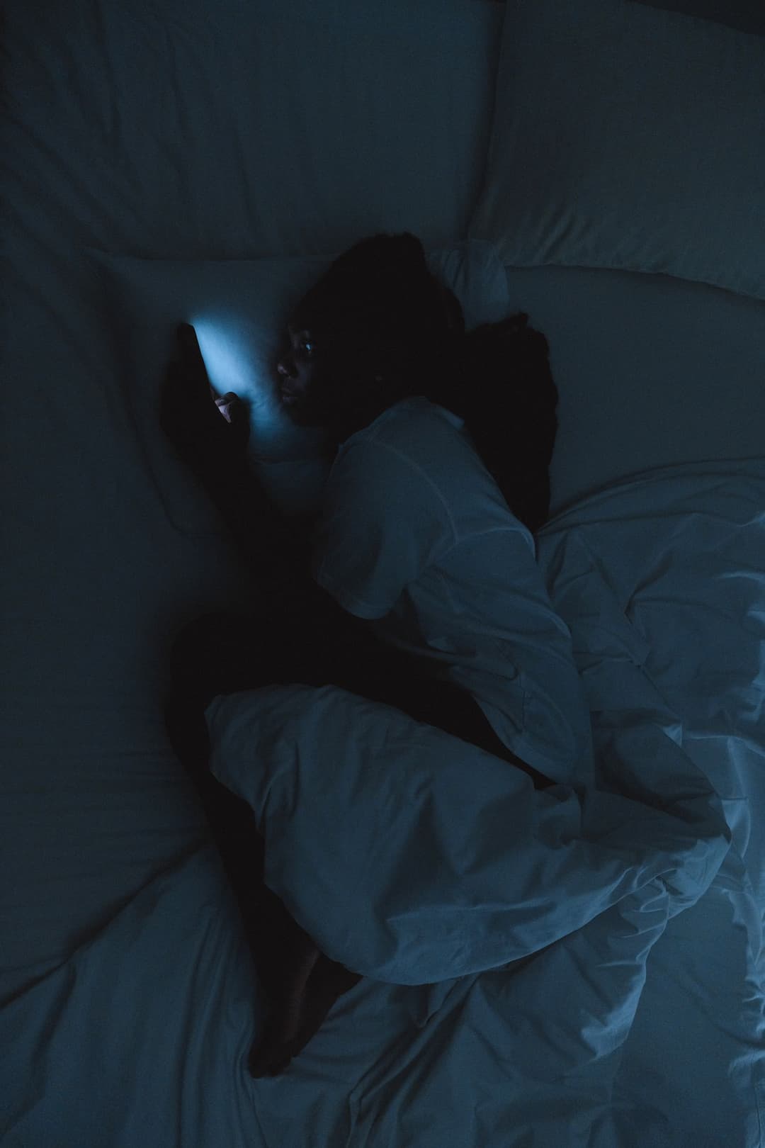 Woman lying in bed at night looking at a smartphone in a dark room