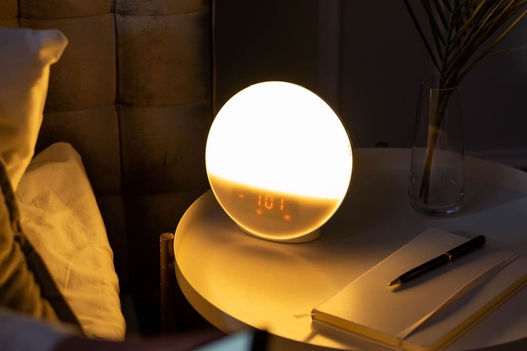 Glowing bedside clock next to a notebook in a dark bedroom