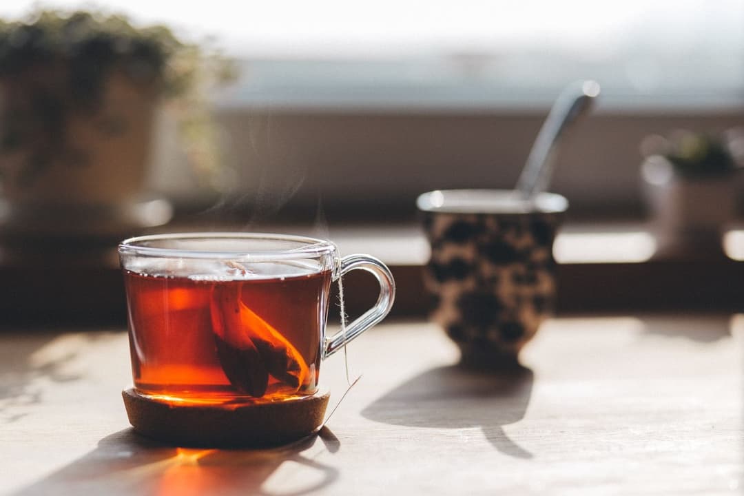 Glass cup of tea with a teabag on a sunlit table by a window
