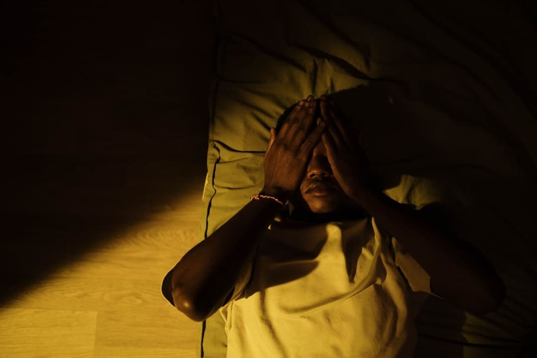 Man lying awake in a dark room with his hands over his face