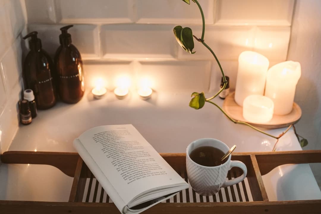 Bath tray with an open book, a cup and lit candles