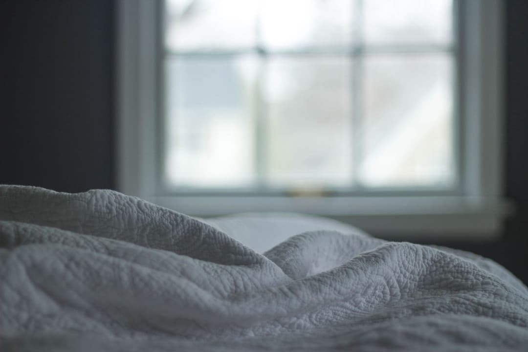 Rumpled grey bed linen beside a bright window