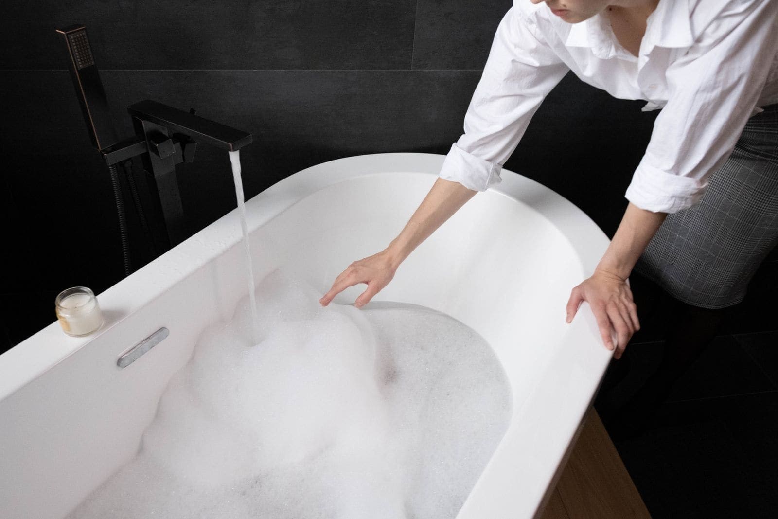 Person running a bath, one hand in the foamy water
