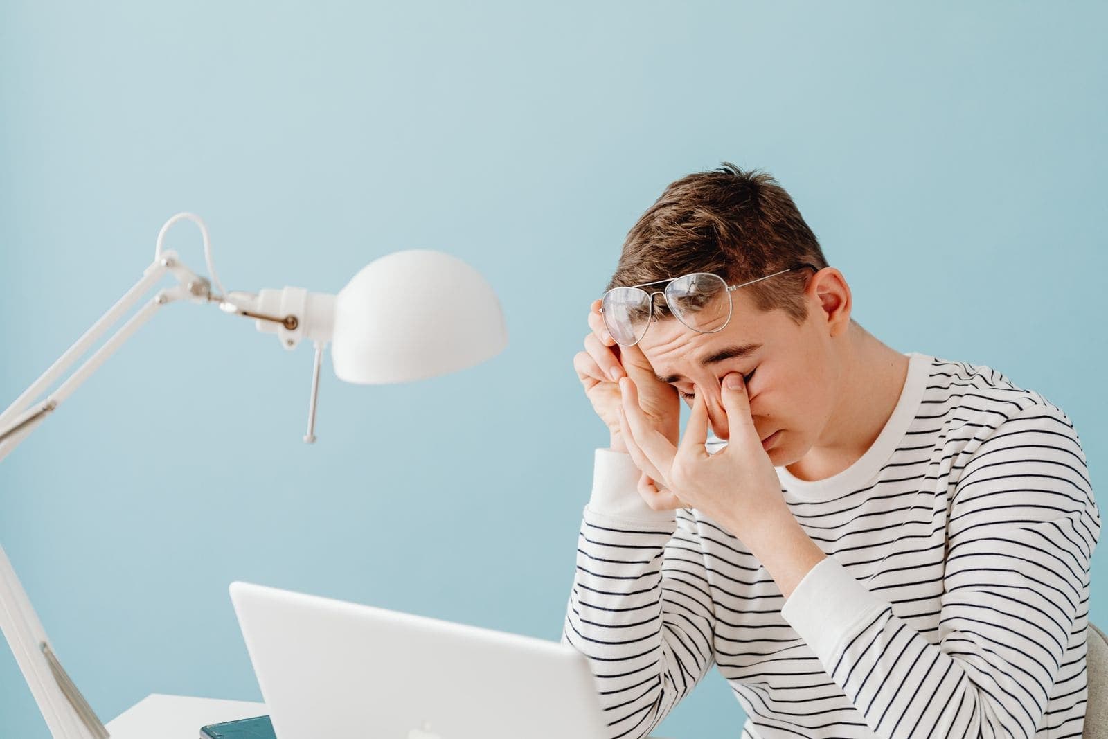 Young man rubbing his eyes at a laptop under a desk lamp