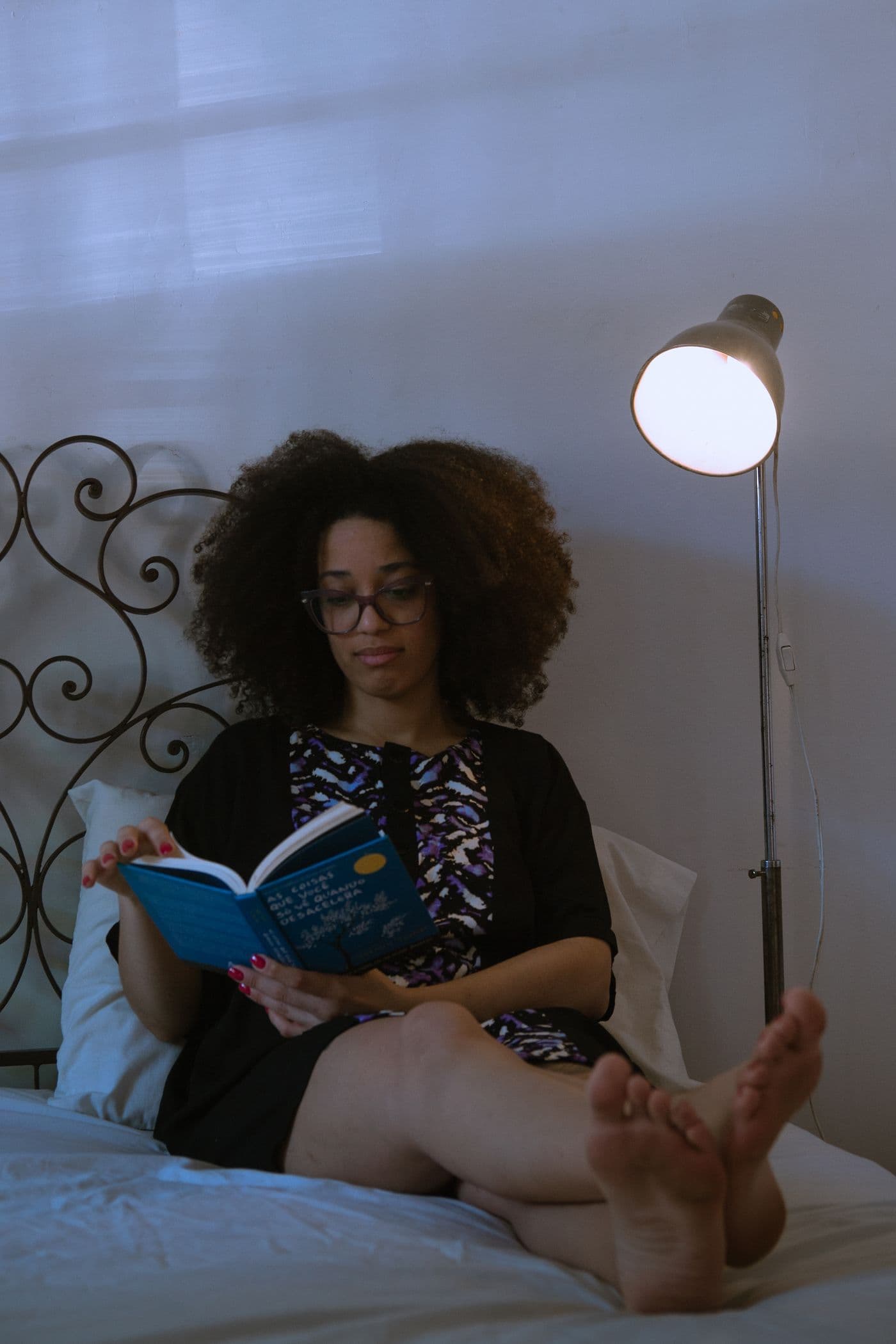 Woman reading on a bed under a floor lamp