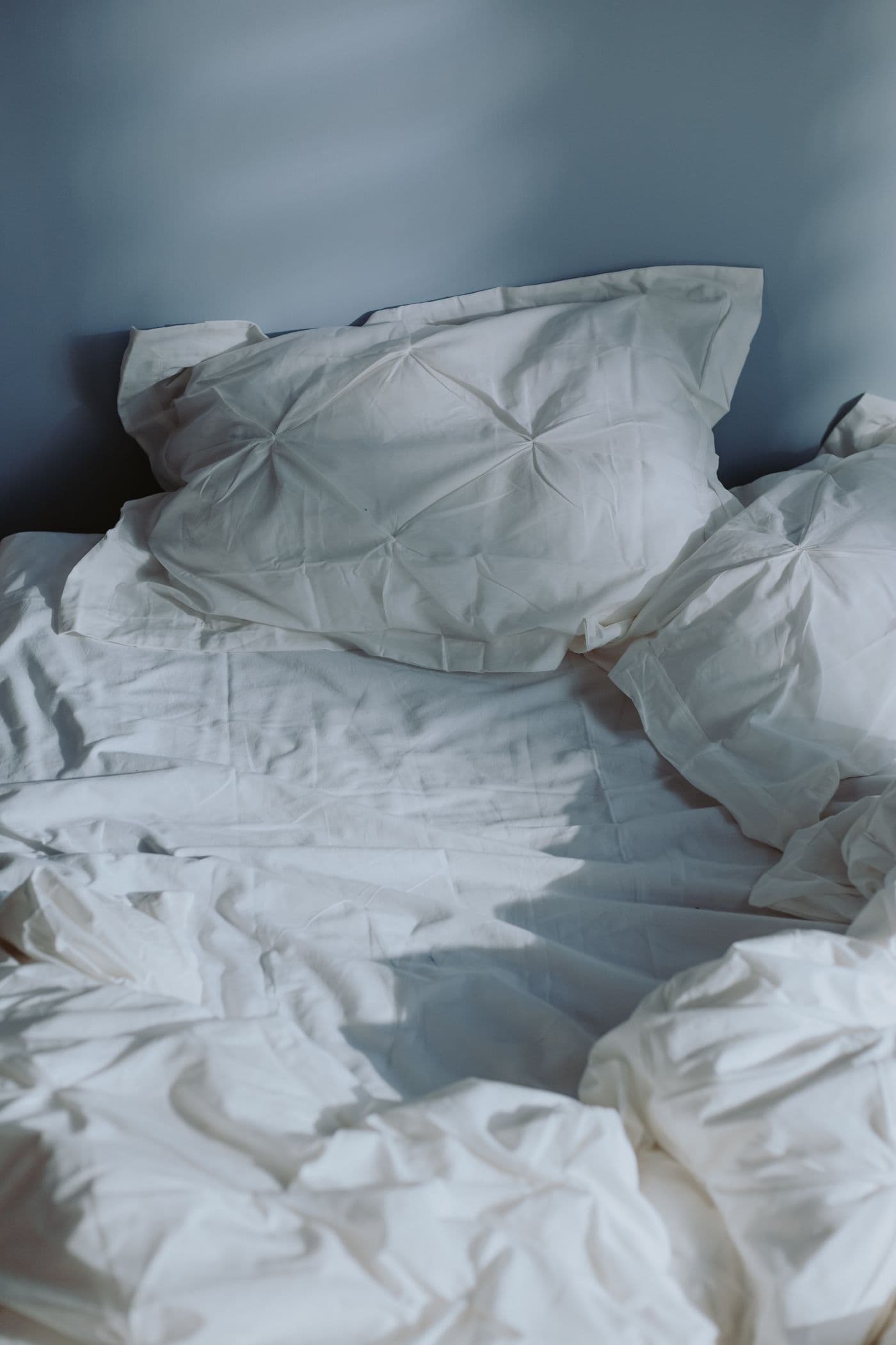 Unmade bed with textured white linens in morning light